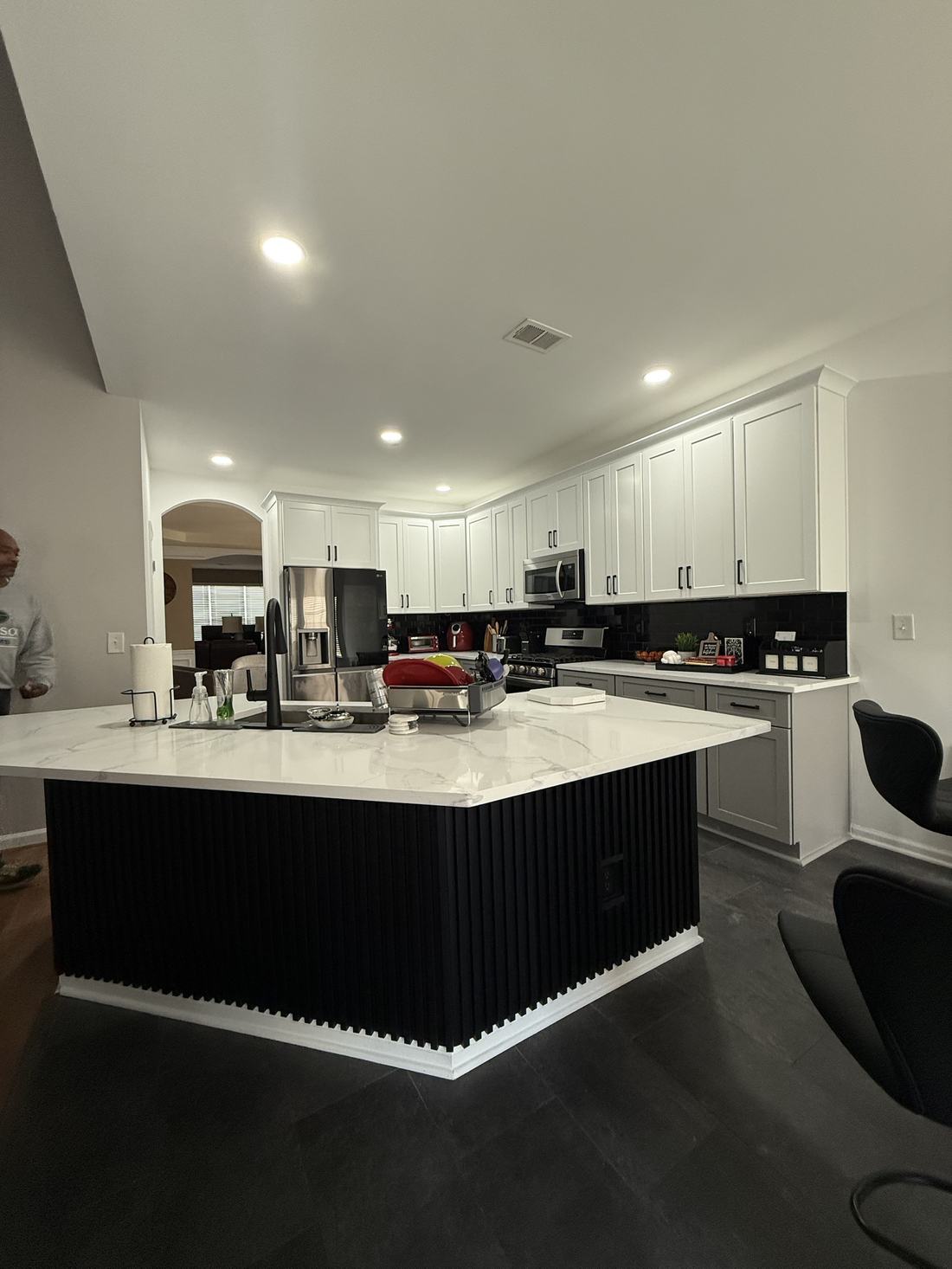 Remodeled kitchen with white shaker cabinets, quartz waterfall island and black fluted panel base